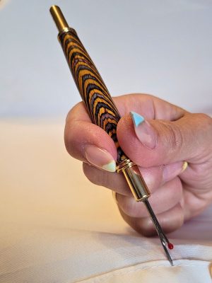 Découd‑vite artisanal en bois lamellé multicolore avec deux dents de coupe plaquées or et système rétractable sécurisé.