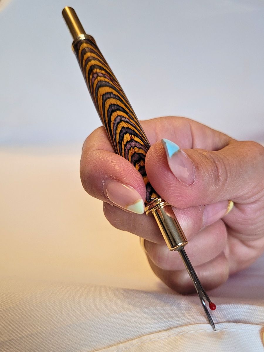 Découd‑vite artisanal en bois lamellé multicolore avec deux dents de coupe plaquées or et système rétractable sécurisé.