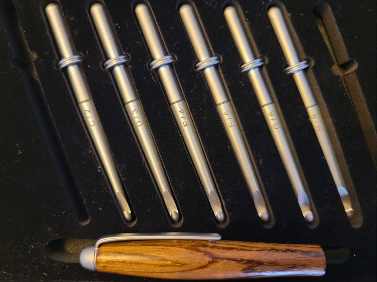 Coffret artisanal de six crochets en aluminium interchangeables sur support en bois serpent, tailles 2 à 8, présentation soignée.