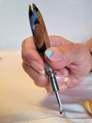 Découd‑vite artisanal hybride en résine époxy bleue et blanche et racine de hêtre, utilisé pour découdre une couture.