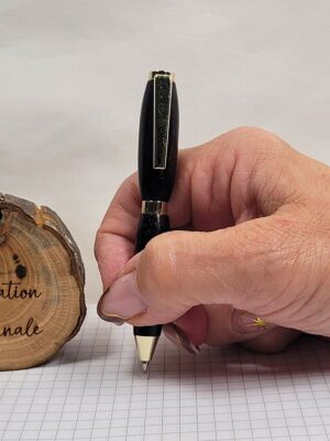 Stylo bille artisanal en ébène avec placage doré, petit format slim mini, tenu en main pour illustrer sa prise en main confortable et ses dimensions compactes.
