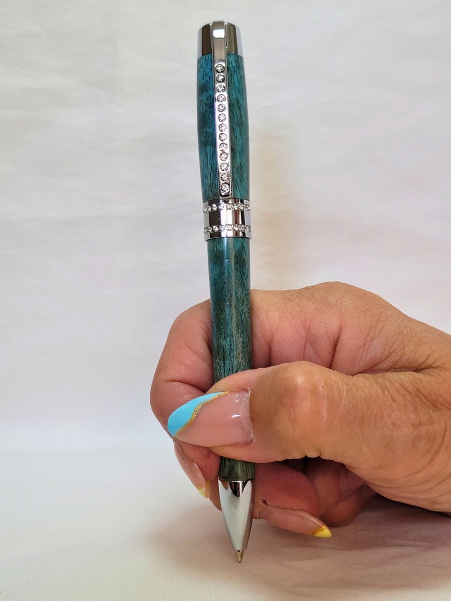 Stylo Princesse bleu aux reflets turquoise tenu en main — stylo artisanal en bouleau, finition chromée et strass blancs, mécanisme twist Parker, élégance et éclat.