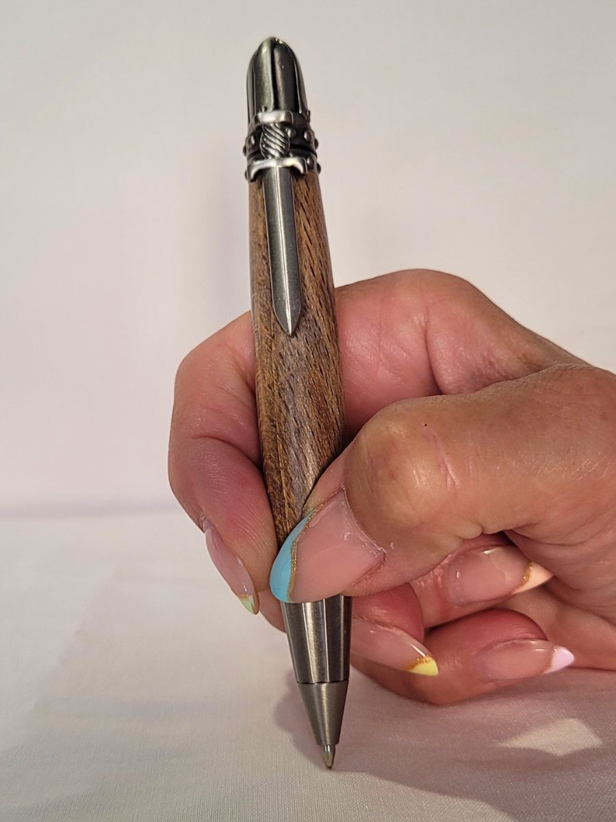 "Main tenant un stylo artisanal en bois avec des finitions métalliques, clip décoratif en forme d'épée, sur fond clair"