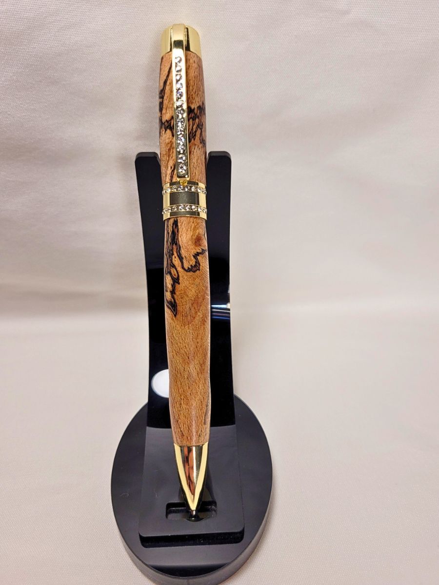 Stylo Princesse en hêtre échauffé sur support noir — stylo artisanal doré, bois veiné et strass blancs, modèle chic pour signatures ou cadeaux élégants.