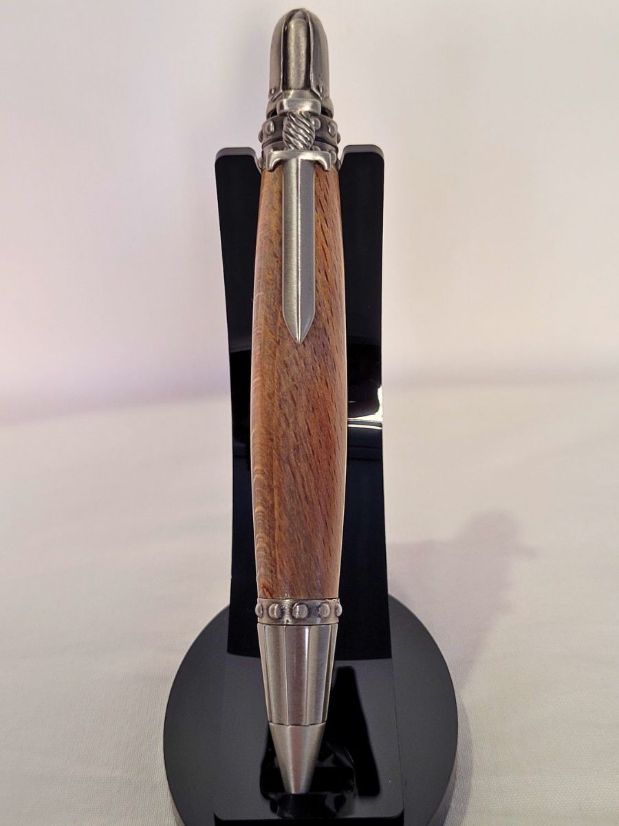 "Stylo bille artisanal médiéval en hêtre avec clip en forme d’épée et casque rotatif, finitions en étain vieilli, présenté sur support noir."