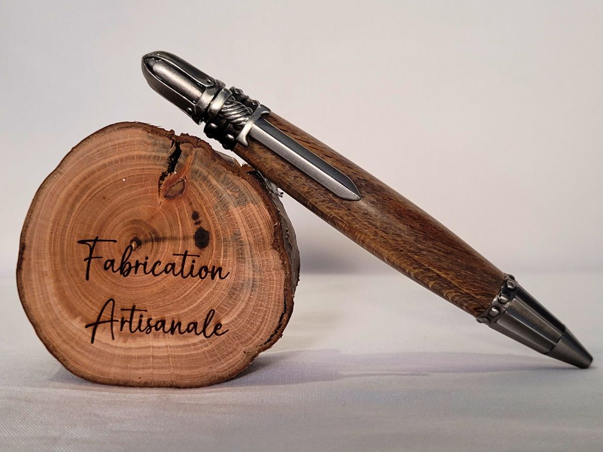 "Stylo médiéval artisanal en hêtre posé sur rondelle de bois gravée Fabrication Artisanale, finitions en étain vieilli et clip épée."