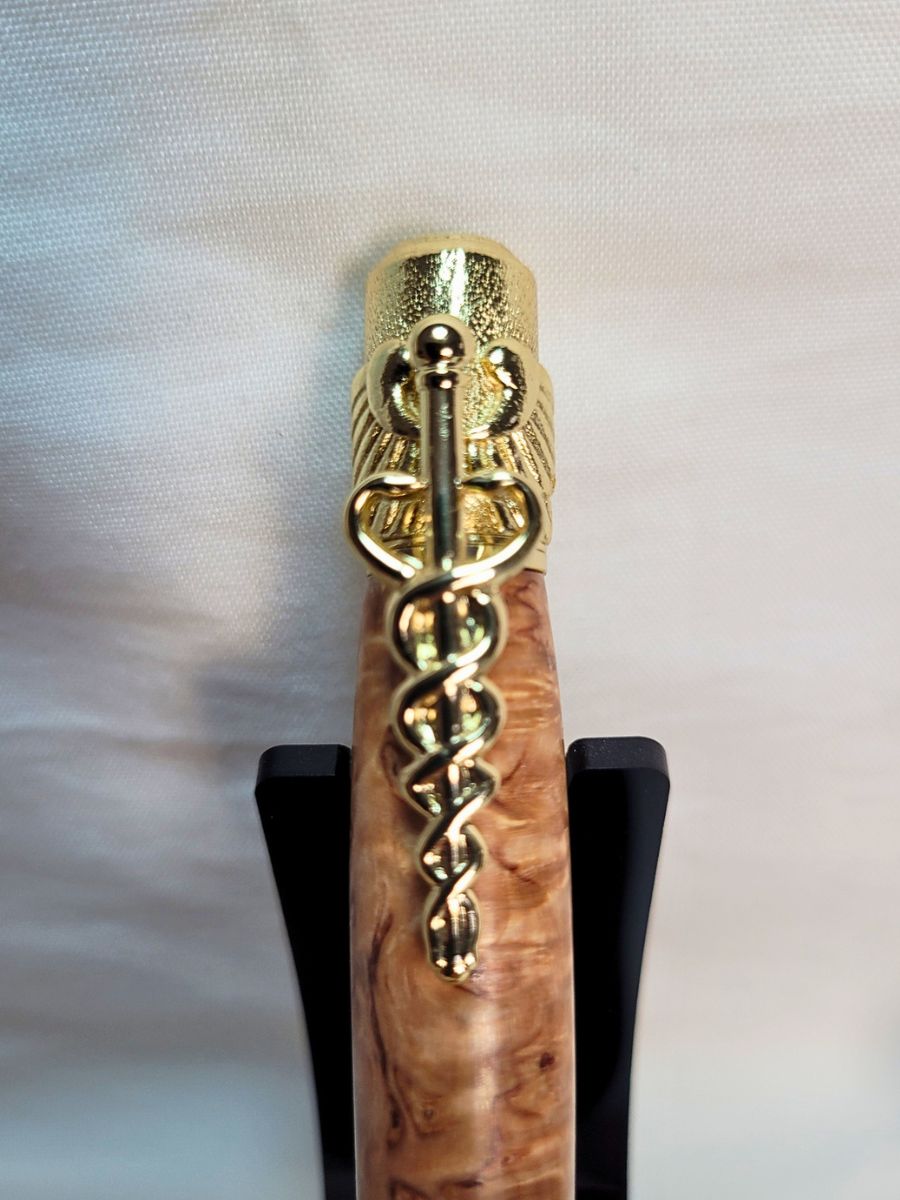 "Détail du haut du stylo médical en loupe de bouleau, placage or avec croix noire et clip caducée finement ciselé."