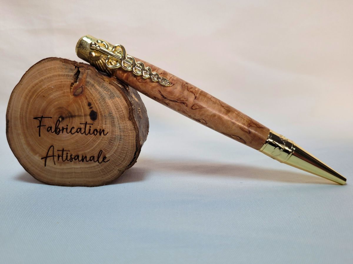 "Stylo médical artisanal en loupe de bouleau avec finitions dorées, posé sur rondelle de bois gravée Fabrication Artisanale."