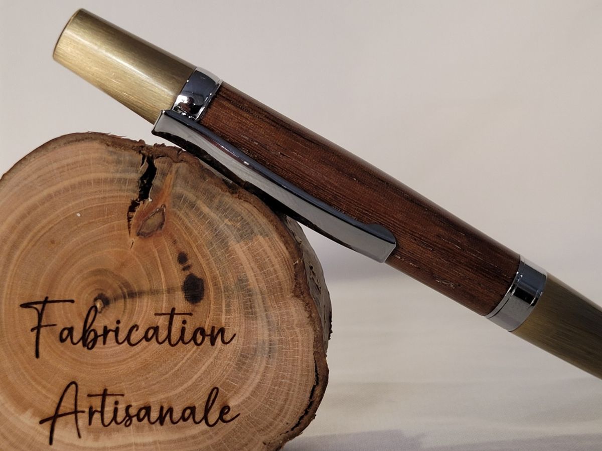Stylo bille artisanal en bois de palmier avec finitions chromées et laiton brossé, posé sur rondin gravé Fabrication Artisanale.