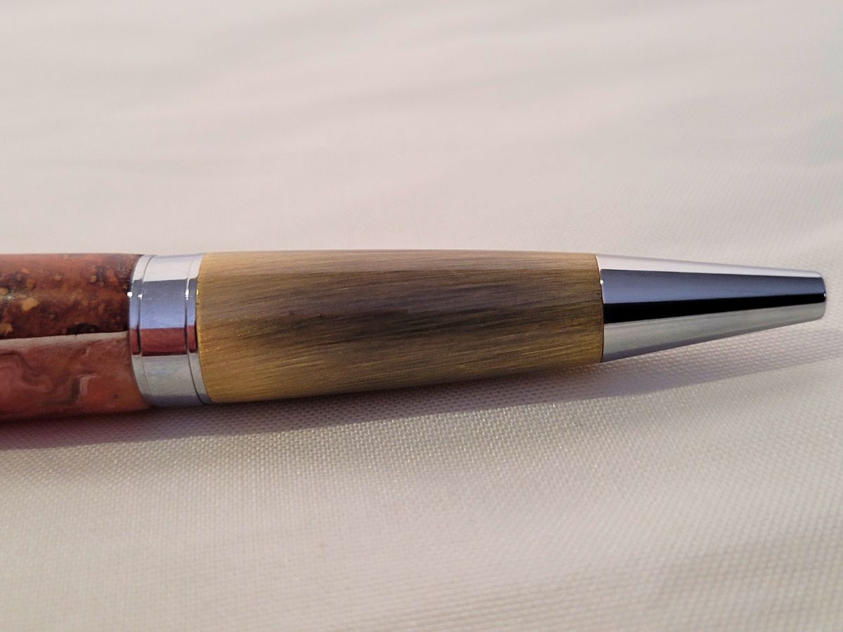 Détail du laiton brossé, de la racine de hêtre et de la résine époxy rose sur stylo bille Élégance artisanal