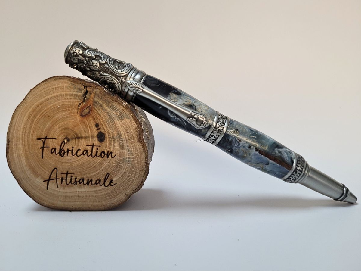 Stylo artisanal en résine époxy bleu et blanc avec copeaux de bois intégrés, présentation artisanale