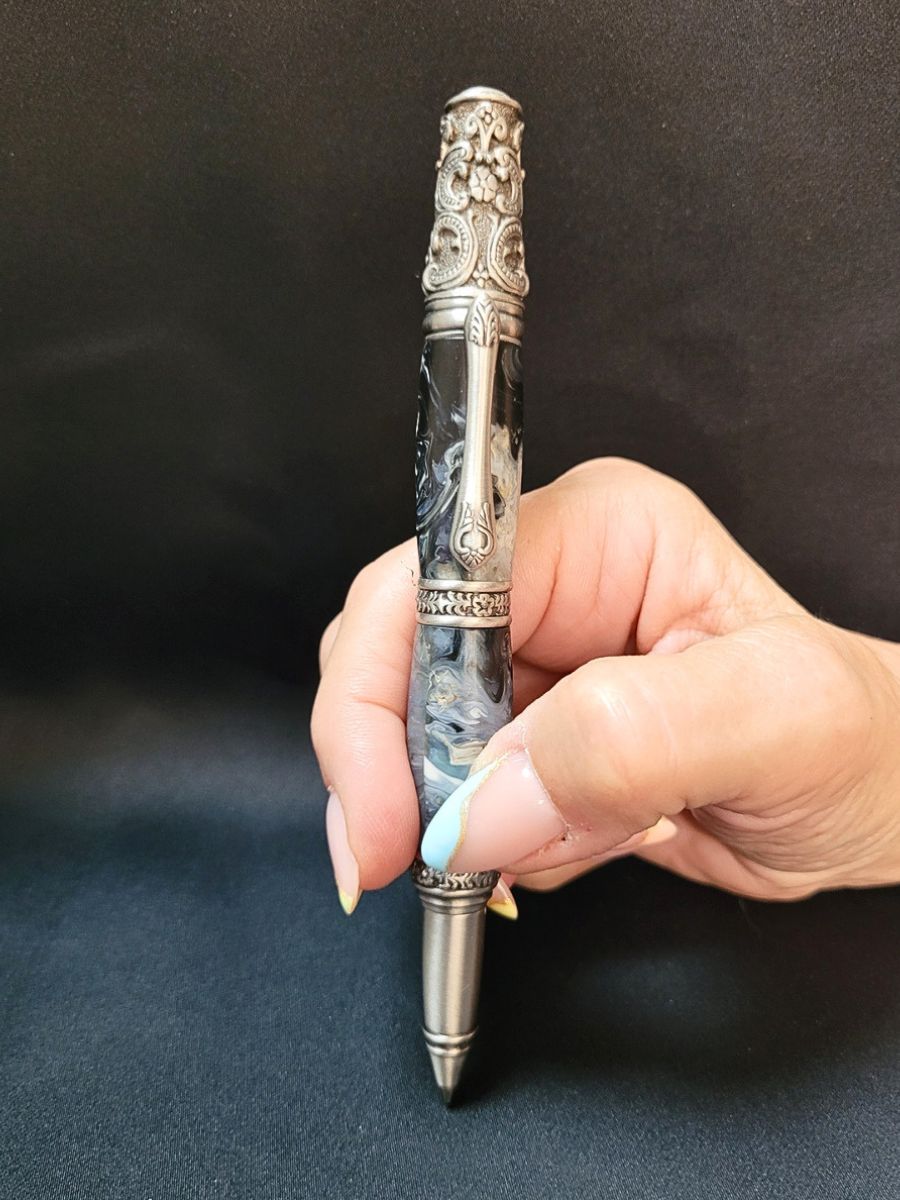 Stylo artisanal en résine époxy bleu et blanc tenu en main, finition étain antique