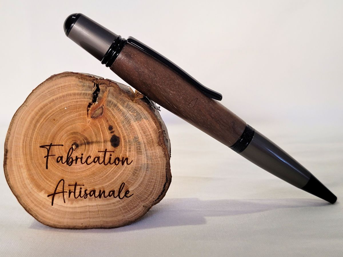 Stylo bille Élégance Cerisier avec finition titane gris et bague noire ciselée présenté sur support artisanal en bois - Atelier du Val des Anges