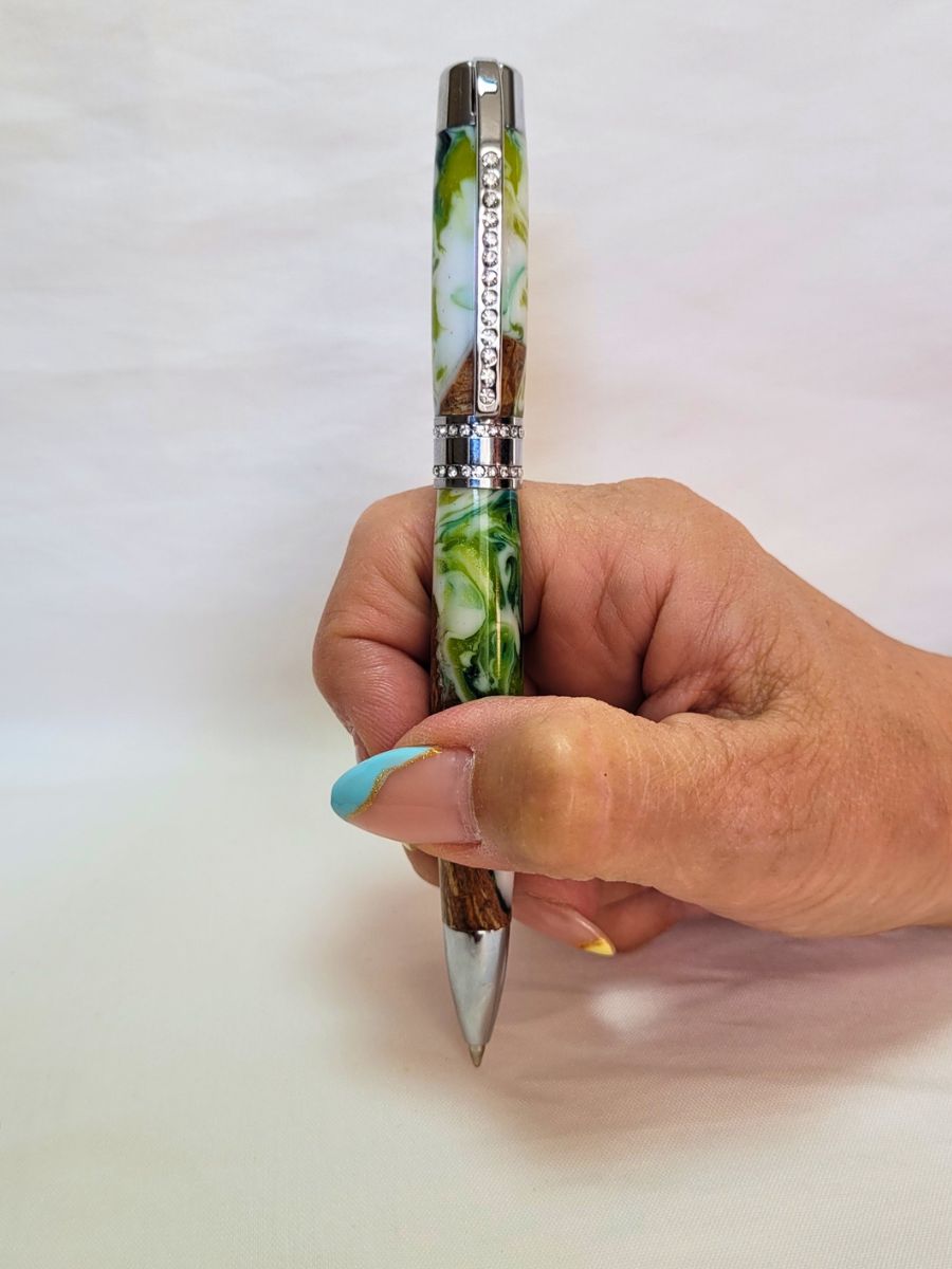 Stylo Princesse hybride tenu en main — stylo artisanal en bois et résine époxy blanc‑vert, finition chrome et strass blancs, confort d’écriture et design raffiné.