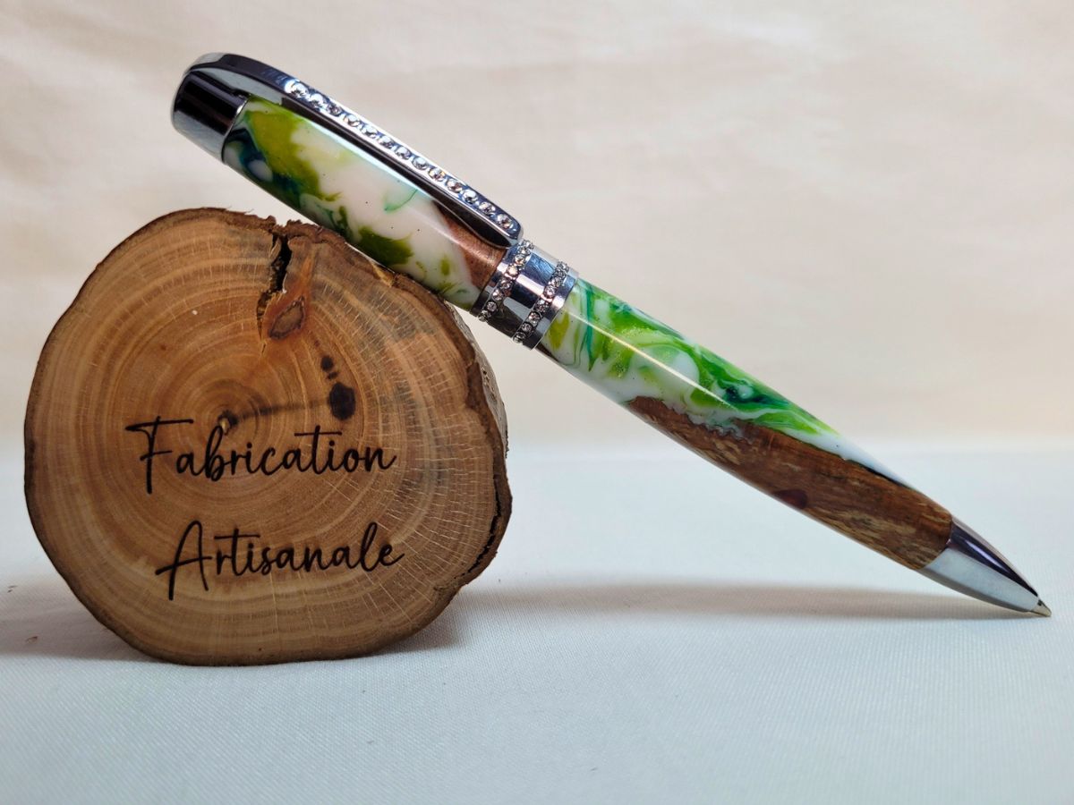 Stylo Princesse hybride posé sur rondin gravé Fabrication artisanale — stylo artisanal en hêtre et résine époxy blanc‑vert, finition chrome et strass blancs, création unique.