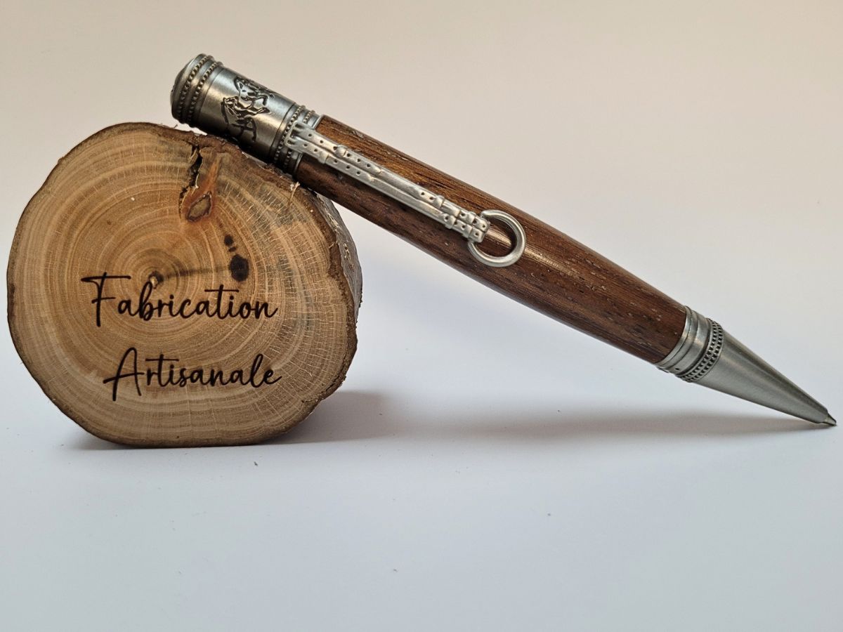 Stylo artisanal en chêne doré posé sur une rondelle de bois gravée Fabrication Artisanale, finitions en étain et clip étrier.