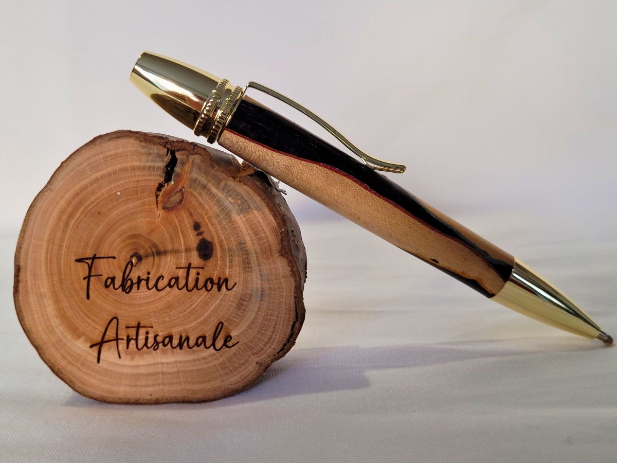 Stylo Alliance en bois de charme et ébène avec placage or posé sur rondin gravé “Fabrication artisanale” – modèle équilibré et raffiné.