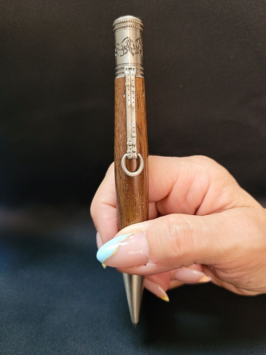 Stylo en chêne doré tenu en main, mécanisme en étain décoré de chevaux au galop et clip étrier, finition artisanale.