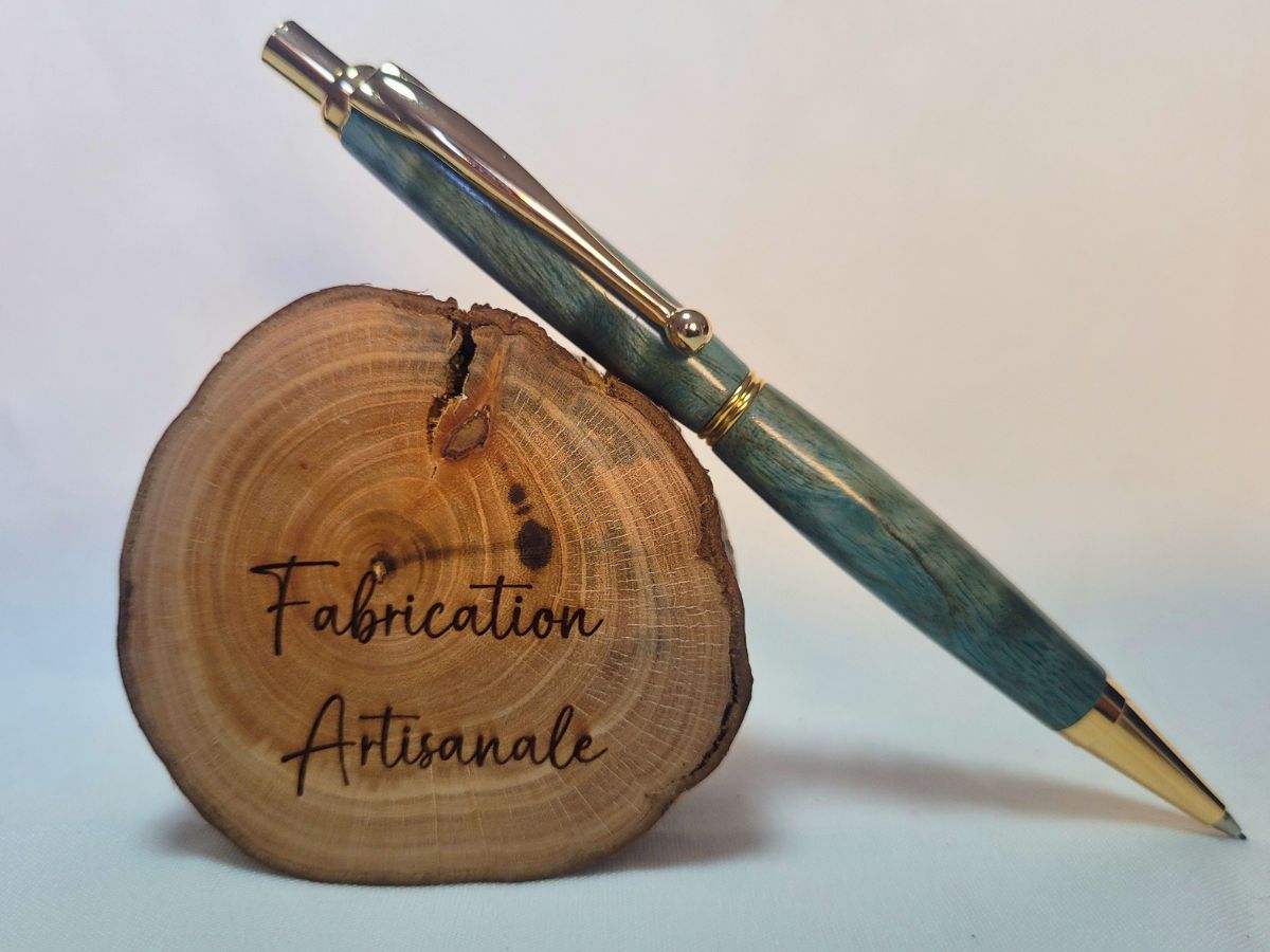 Porte‑mine artisanal en bois de bouleau teinté bleu avec placage doré, posé sur rondin gravé « Fabrication Artisanale »
