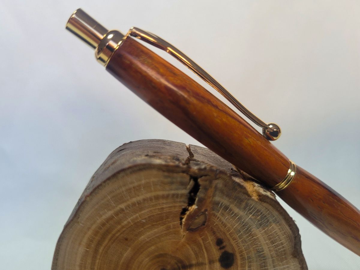 Porte‑mine artisanal en bois de padouk avec détails dorés, posé sur rondin naturel