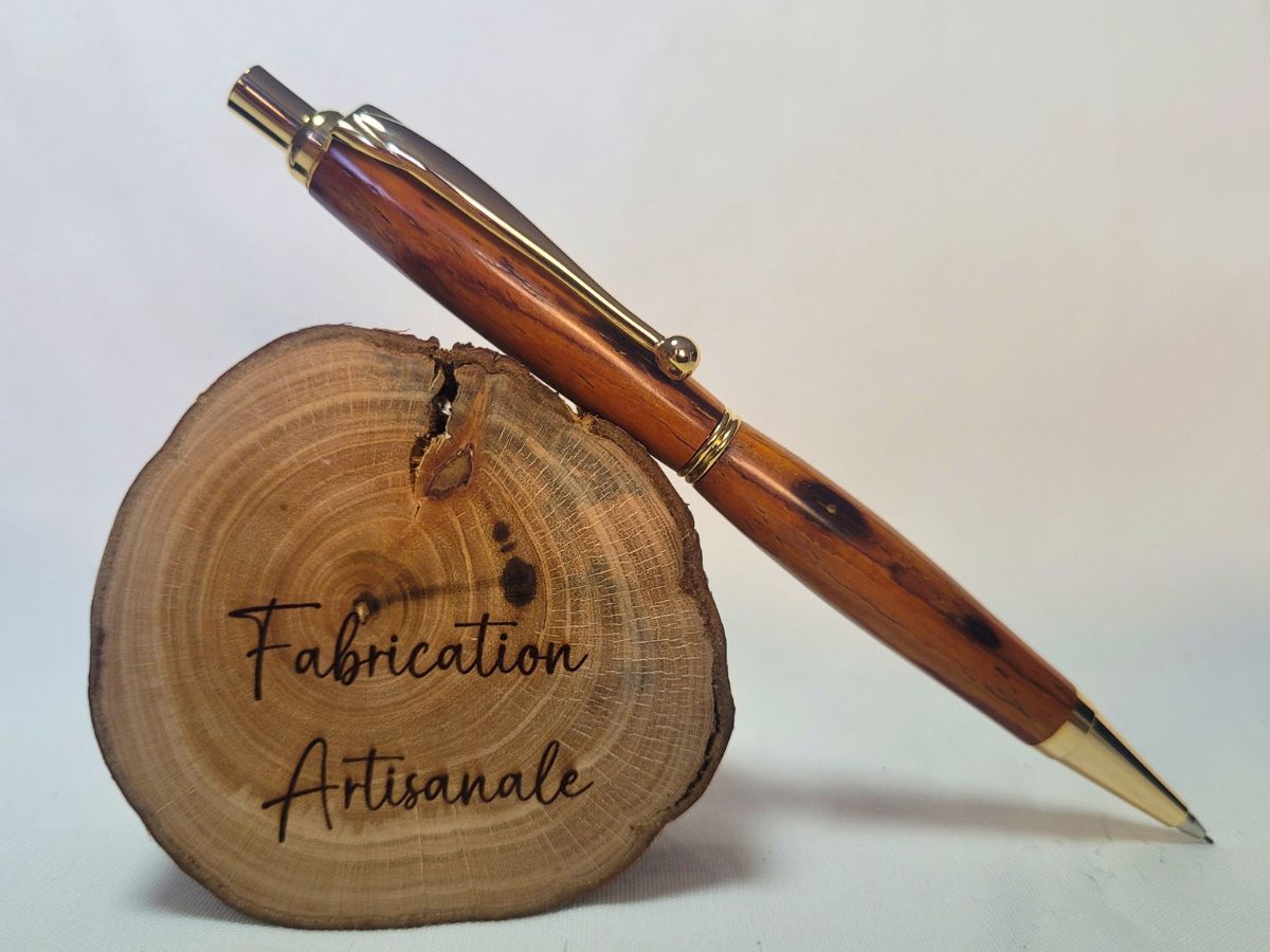 Porte‑mine en bois de padouk, placage doré, fabrication artisanale française, posé sur rondin gravé « Fabrication Artisanale »