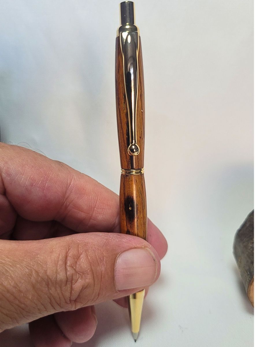 Porte‑mine artisanal en bois de padouk avec placage doré, tenu en main pour montrer la finition brillante