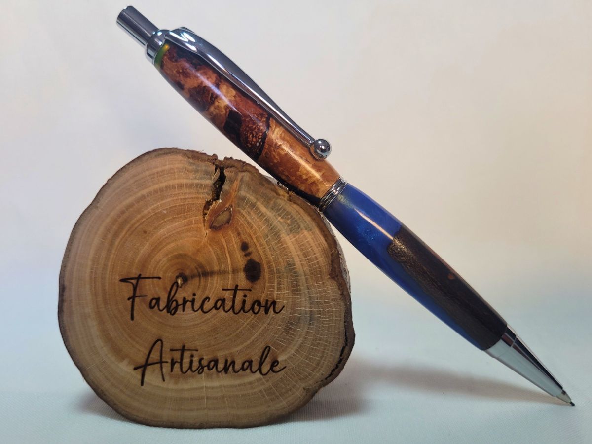 Porte‑mine artisanal en racine de hêtre et résine époxy bleue, placage chromé, posé sur rondin gravé « Fabrication Artisanale »