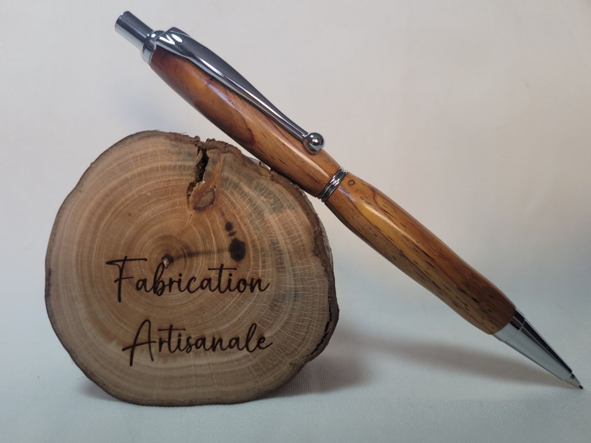 Porte‑mine en bois de padouk, finition chromée, fabrication artisanale, posé sur rondin gravé « Fabrication Artisanale »