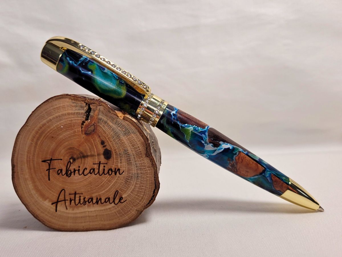 Stylo hybride en hêtre et résine époxy bleu-blanc, finition dorée et strass blancs, posé sur rondin gravé Fabrication artisanale.