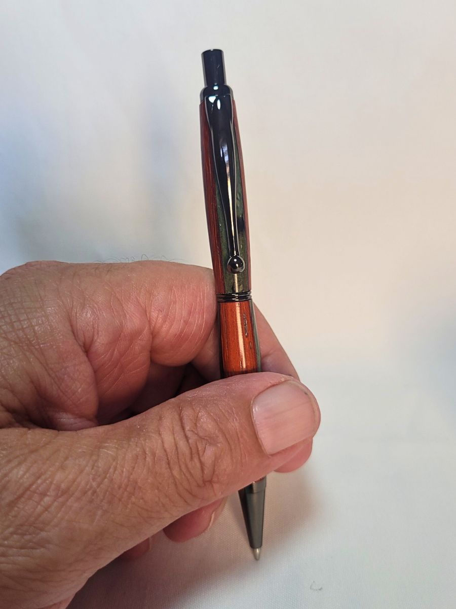 Porte‑mine artisanal en padouk, hêtre teinté bleu et placage noir, finition noire brillante, mécanisme clic, tenu en main pour démontrer la prise en main.