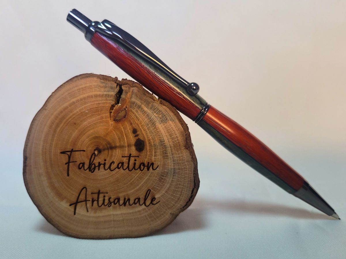 Porte‑mine artisanal en padouk, hêtre teinté bleu et placage noir, finition noire, posé sur rondin gravé « Fabrication artisanale ».