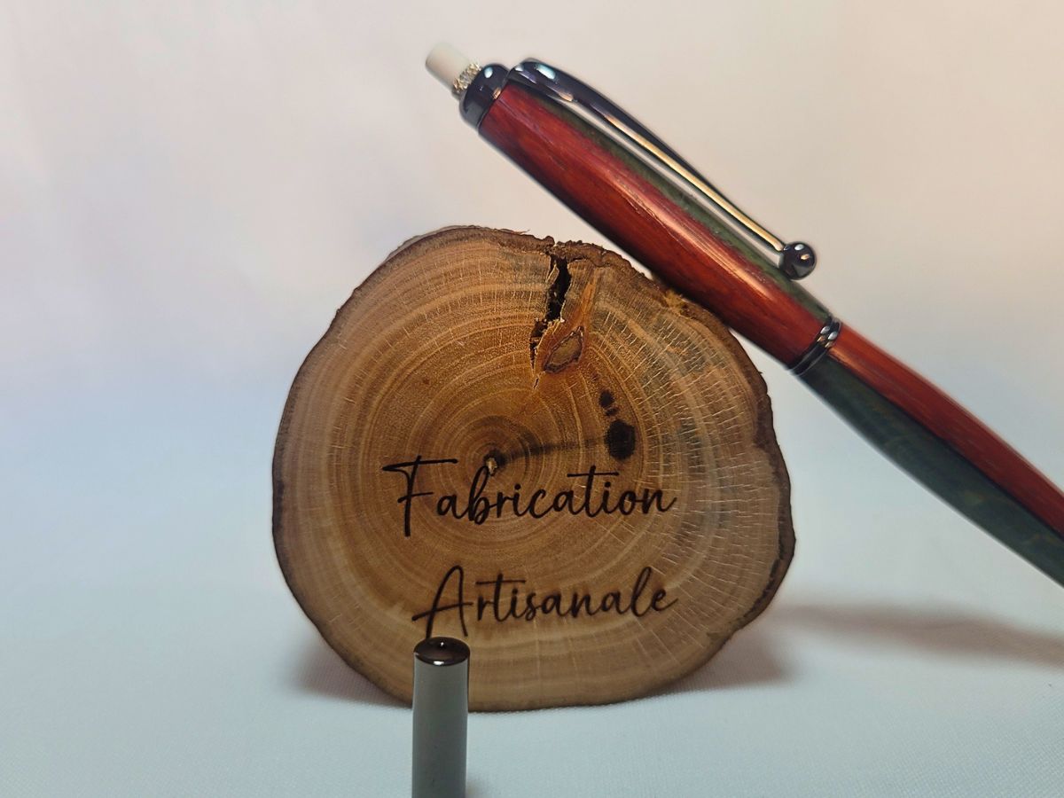 Porte‑mine artisanal en padouk, hêtre teinté bleu et placage noir, gomme intégrée visible, sur rondin « Fabrication artisanale ».