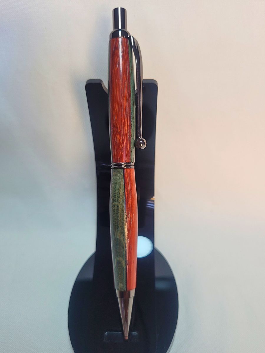 Porte‑mine artisanal en padouk, hêtre teinté bleu et placage noir, finition chromée avec épingle boule et mécanisme clic, sur support noir.