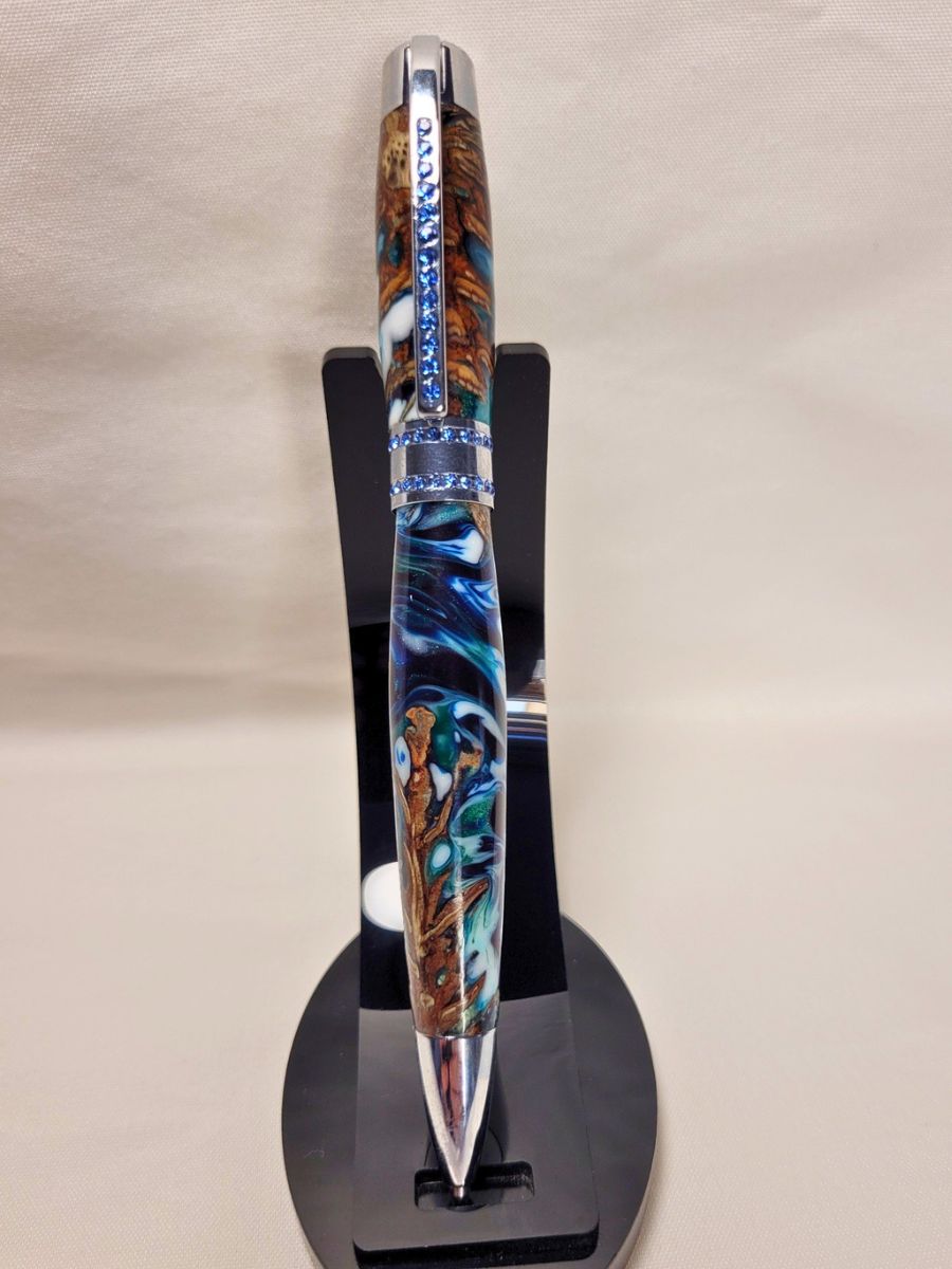 Stylo artisanal Princesse en pomme de pin et résine époxy bleu-blanc-émeraude, finition chrome et strass bleus, présenté sur support noir.