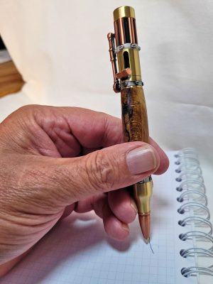 "Stylo steampunk en hêtre échauffé tenu en main, levier en cuivre et pointe en laiton façon balle"