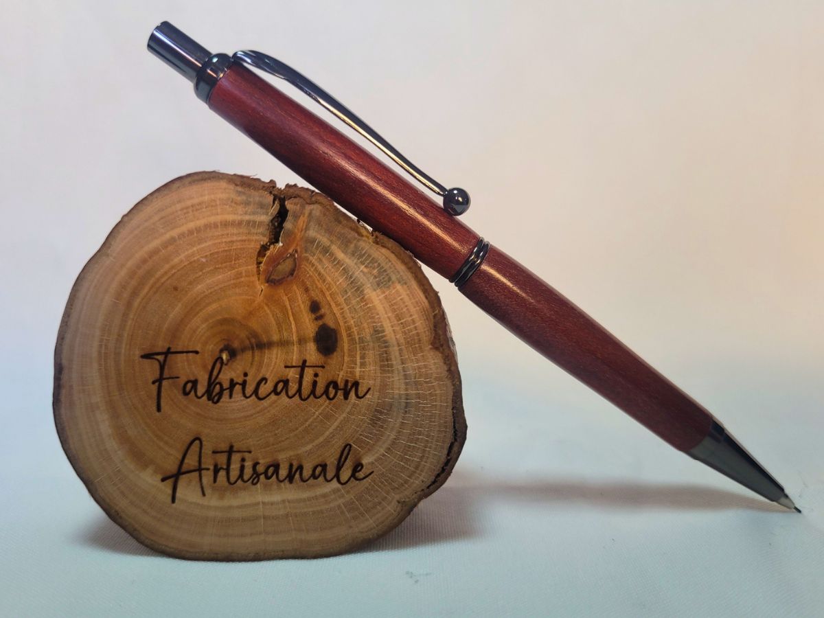 Porte‑mine artisanal en bois de Cœur rouge, finition noire brillante, posé sur rondin gravé « Fabrication artisanale ».