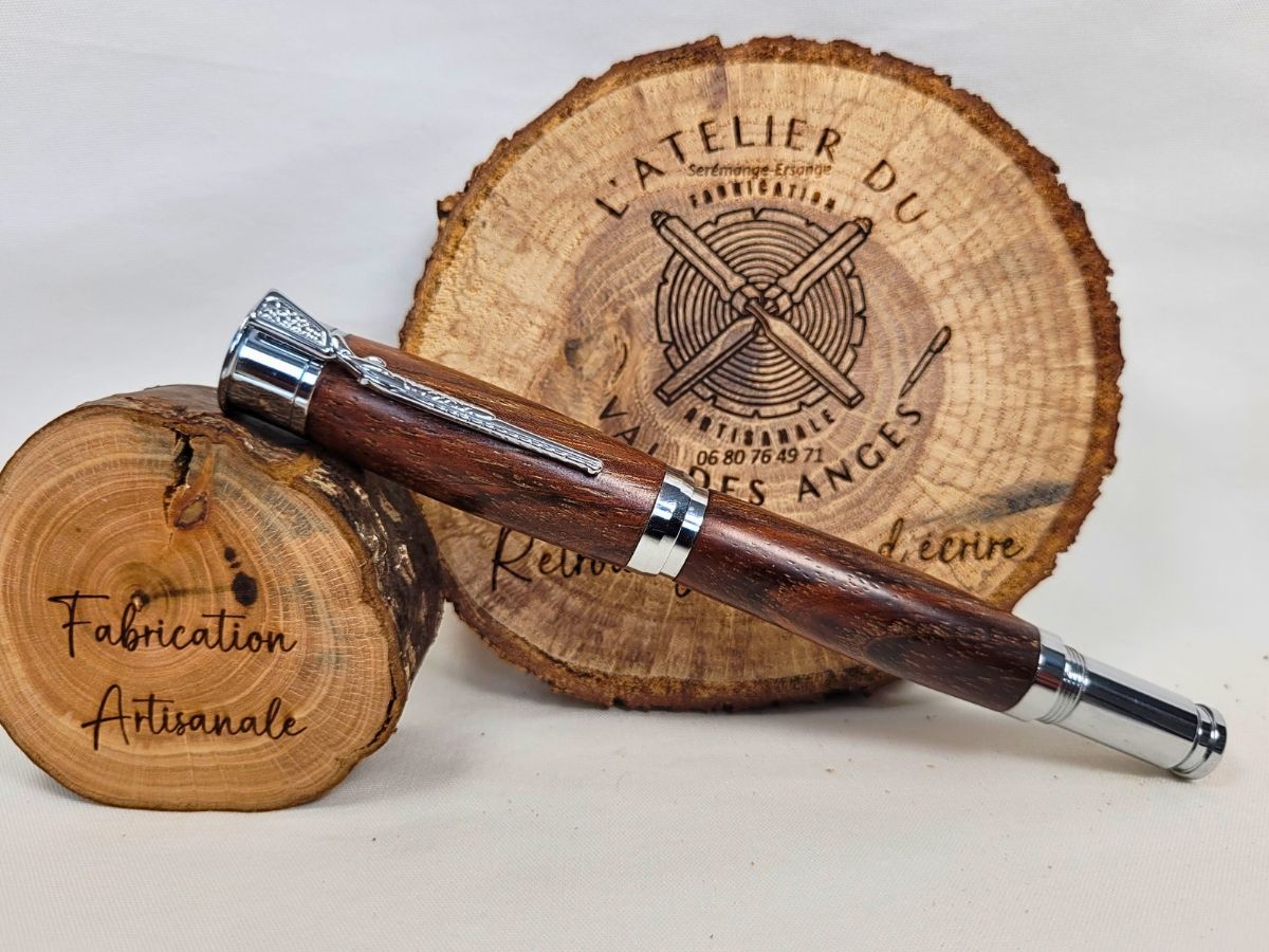Stylo roller artisanal en palissandre avec finitions chromées, présenté sur des rondins de bois dans un atelier de fabrication française