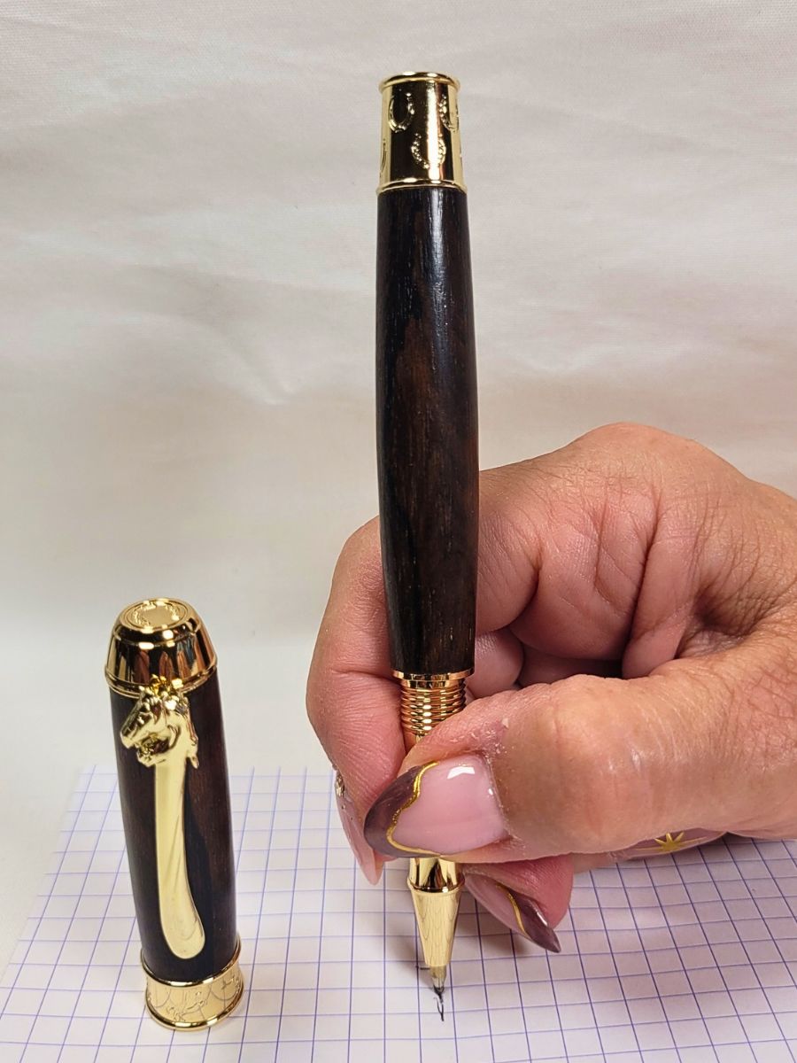 Stylo roller de luxe en wacapou avec décor équestre doré, fers à cheval ciselés et écriture céramique fluide tenu en main
