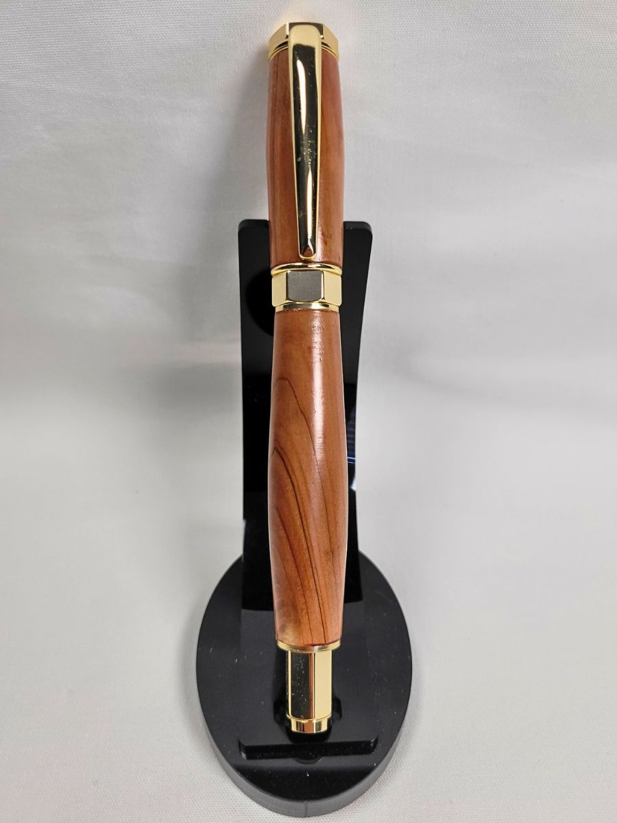 Stylo roller artisanal en bois de genévrier avec placage or, présenté debout sur support, veinures naturelles uniques et capuchon magnétique.