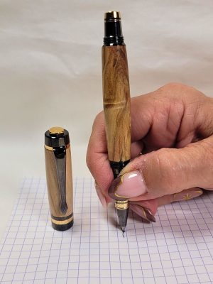 Roller en bois de bouleau noir et or en situation d'écriture, équipé d'une pointe roller céramique offrant une écriture fluide, précise et confortable au quotidien