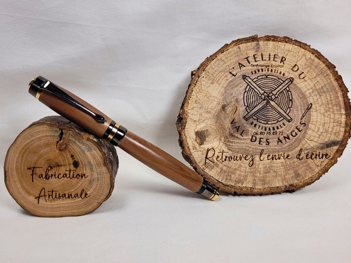 Roller artisanal en bois de prunier noir et or avec capuchon vissé et finitions haut de gamme posé sur un rondin de bois