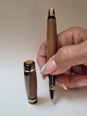 Stylo roller artisanal en prunier avec finition noire brillante et bagues dorées élégantes tenu en main