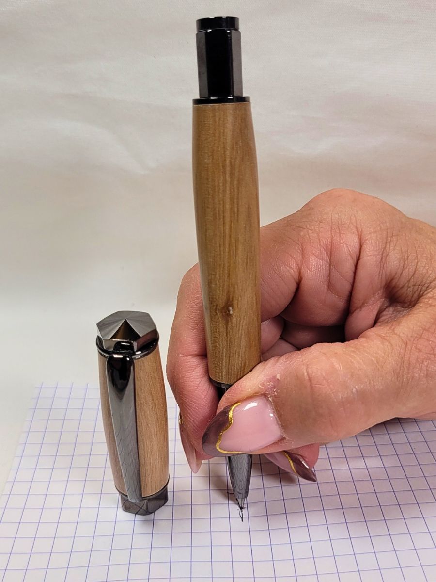 Stylo roller artisanal en bois de prunier avec finition noire hexagonale en cours d'utilisation
