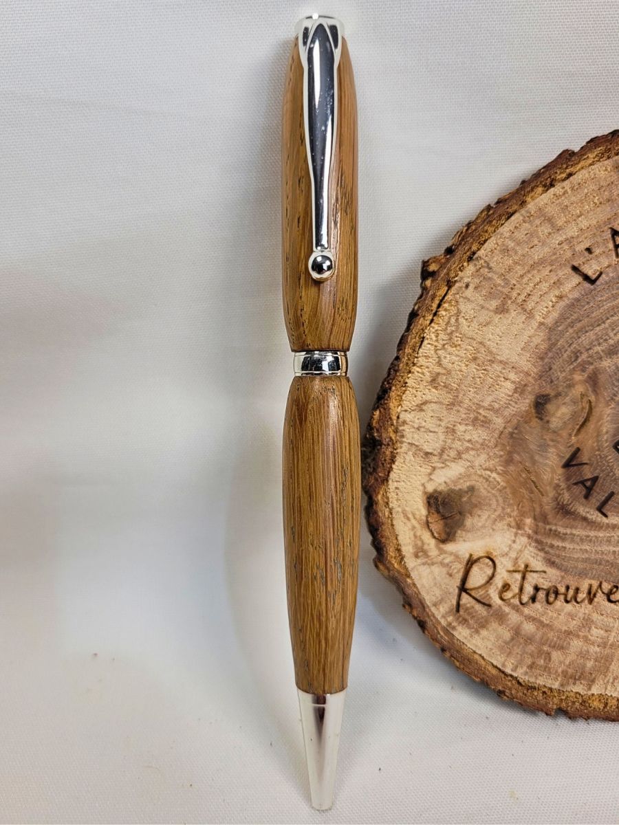 Stylo slim artisanal en chêne massif, placage chrome brillant, épingle à boule, présenté verticalement sur fond clair.