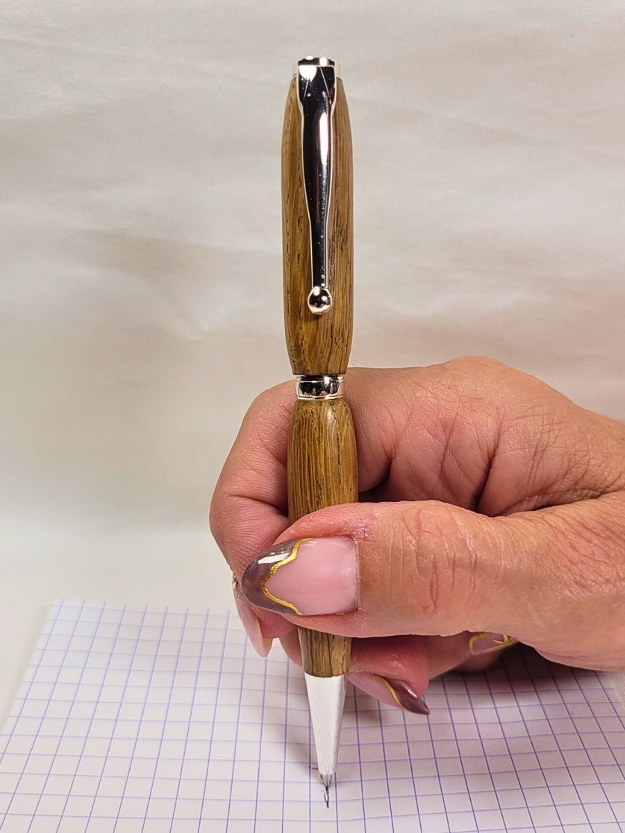 Stylo slim en chêne massif et chrome brillant tenu en main, démonstration d’écriture sur papier quadrillé.