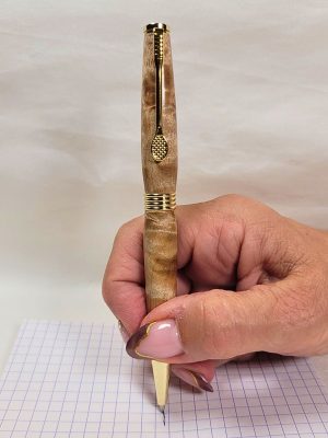 Stylo bille en bois de bouleau ondé avec clip raquette doré, tenu en main lors de l’écriture sur papier quadrillé.