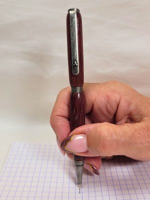 Stylo artisanal en bois d’amarante et étain massif tenu en main, démonstration d’écriture sur papier quadrillé.