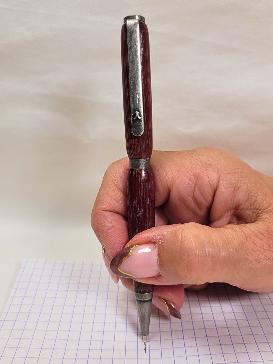 Stylo artisanal en bois d’amarante et étain massif tenu en main, démonstration d’écriture sur papier quadrillé.