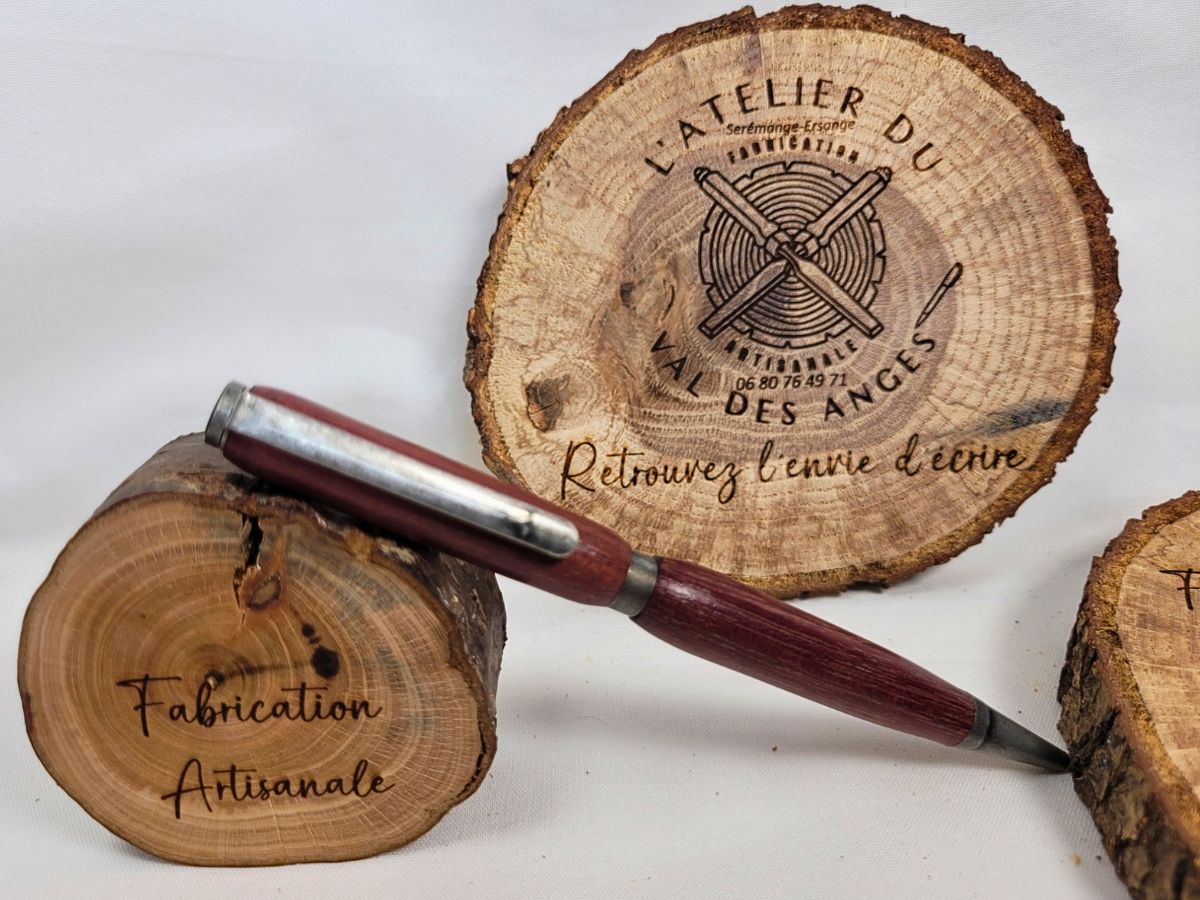 Stylo slim en amarante de Guyane, étain massif et sigle lambda, posé sur rondin gravé Fabrication artisanale, logo L’Atelier du Val des Anges.