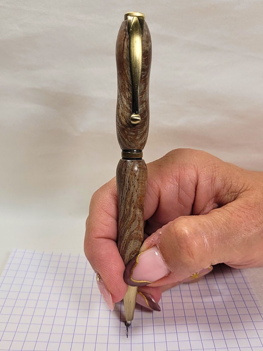 Stylo slim en racine de hêtre et bronze antique tenu en main, démonstration d’écriture sur papier quadrillé.
